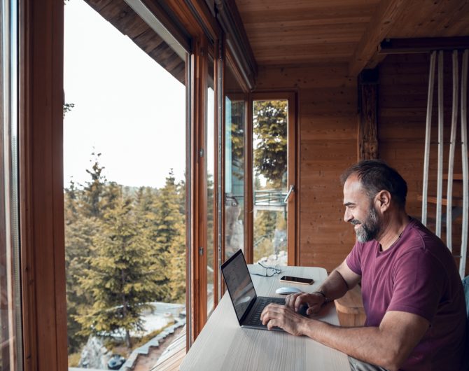 Close up of a mid adult man working on a laptop from his cabin in the woods