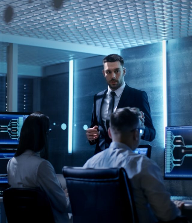 Supervisor Holds Briefing for His Employees in System Control Center Full of Monitors and Servers. Possibly Government Agency Conducts Investigation.