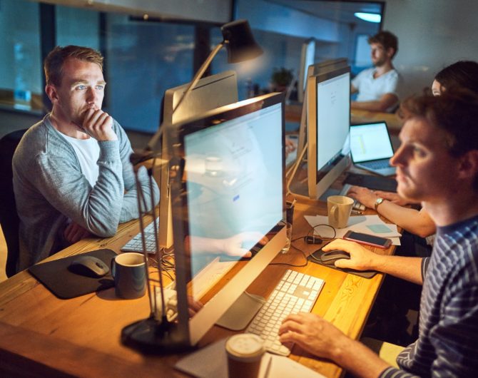 Shot of a group of young people using computers during a late night in a modern office